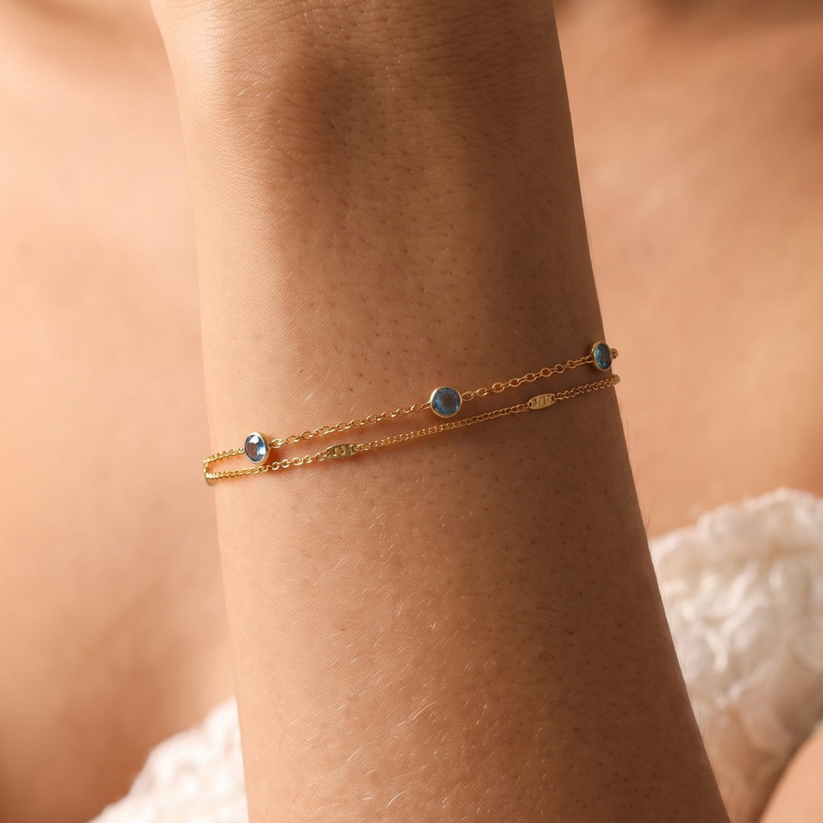 Close-up of the Lagoon Bracelet on the wrist, featuring delicate gold chains with blue bezel-set crystals