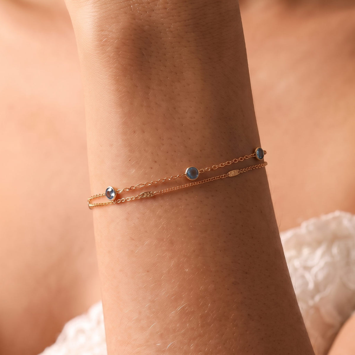 Close-up of the Lagoon Bracelet on the wrist, featuring delicate rose gold chains with blue bezel-set crystals