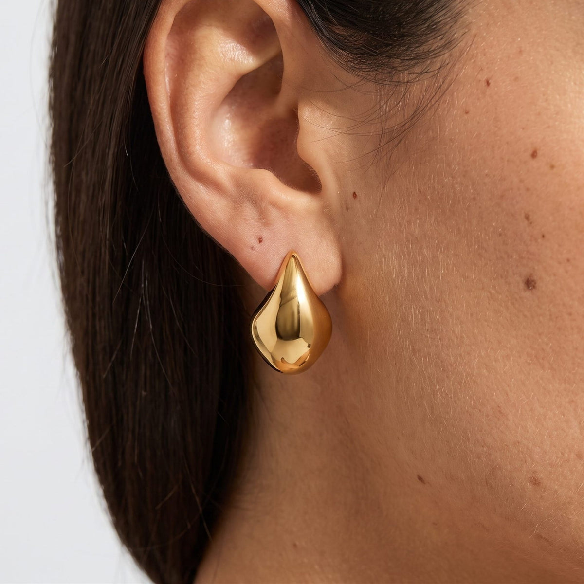 Woman wearing the Lena Curved Hoop Earrings, a chunky gold teardrop shape on the lobe