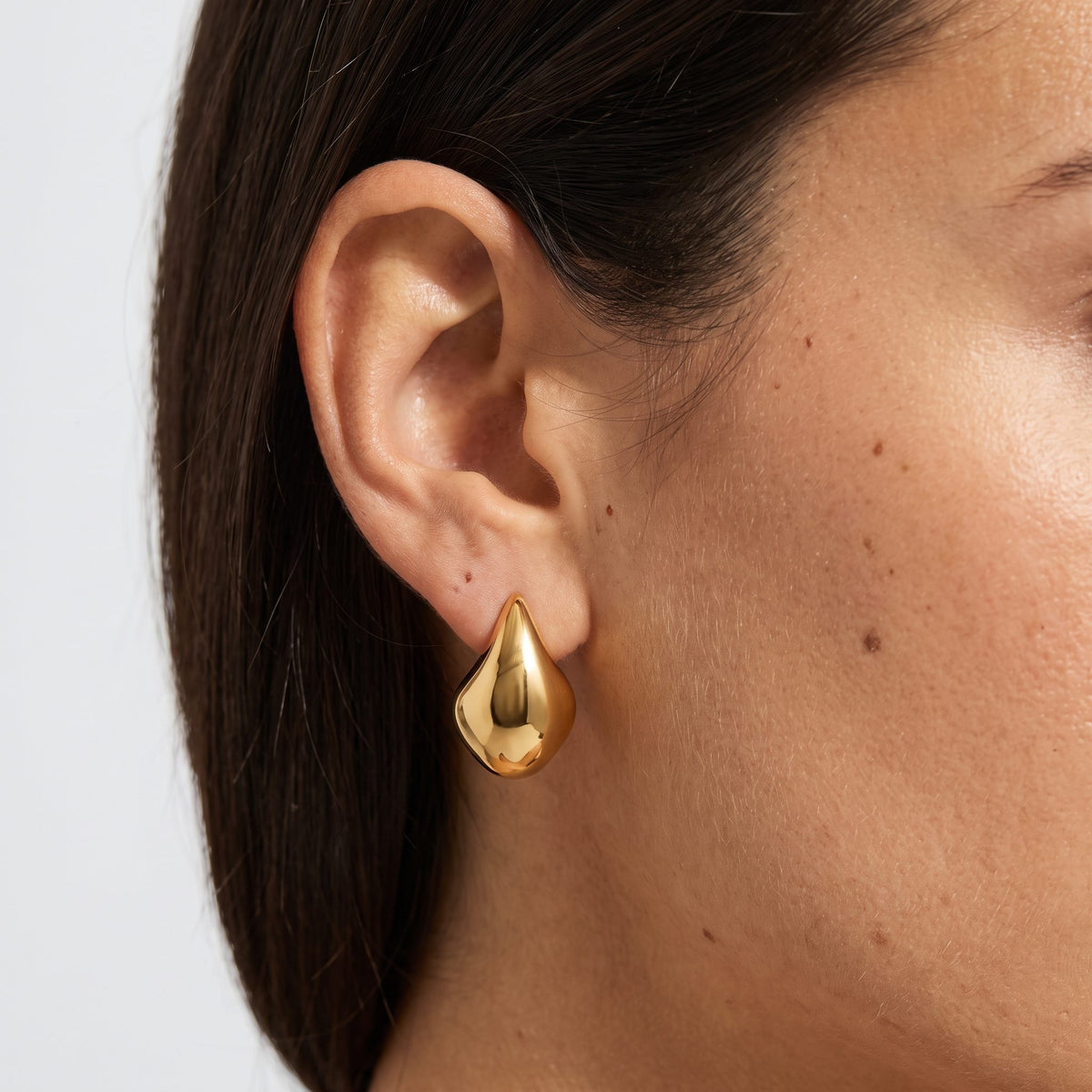 Woman wearing the Lena Curved Hoop Earrings, a chunky gold teardrop shape on the lobe