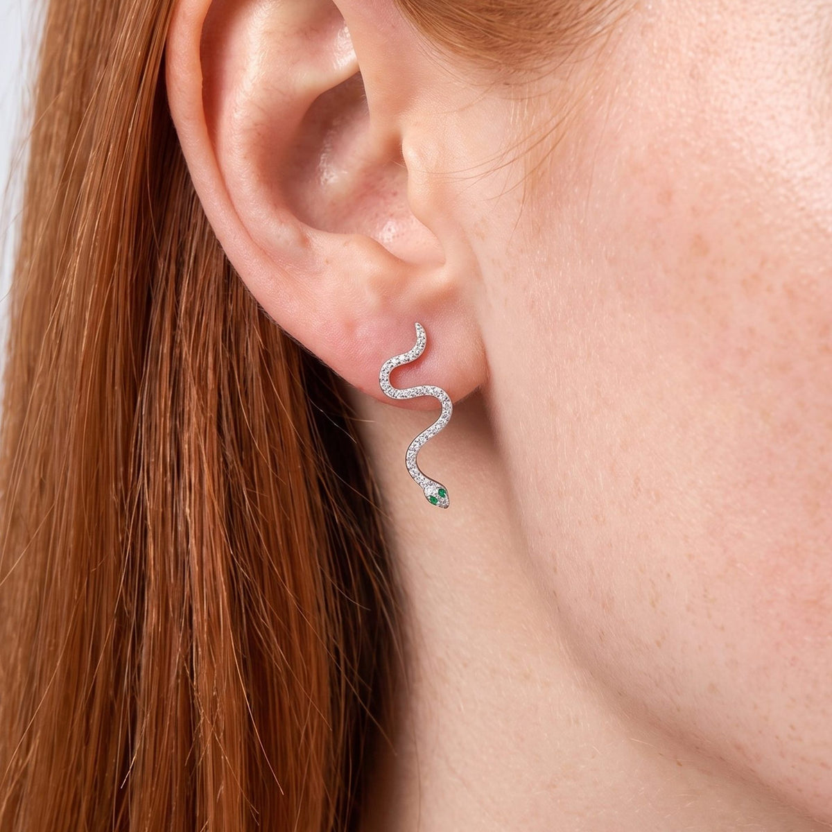 Woman wearing the Liana Crystal Snake Earrings on her lobe, which curves down with a tiny green eye