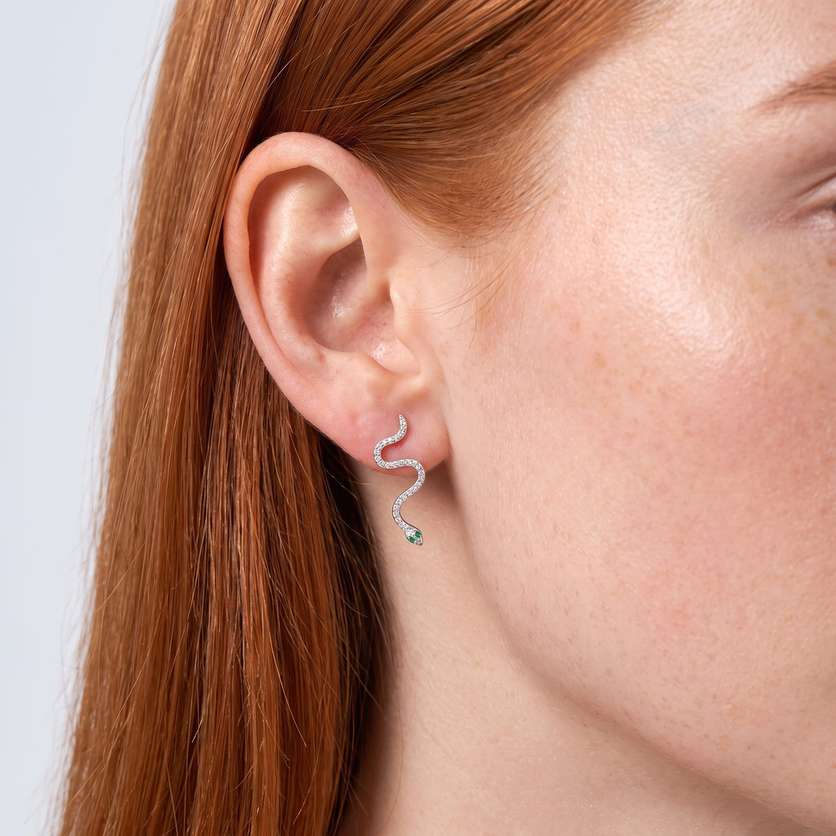 Woman wearing the Liana Crystal Snake Earrings on her lobe, which curves down with a tiny green eye