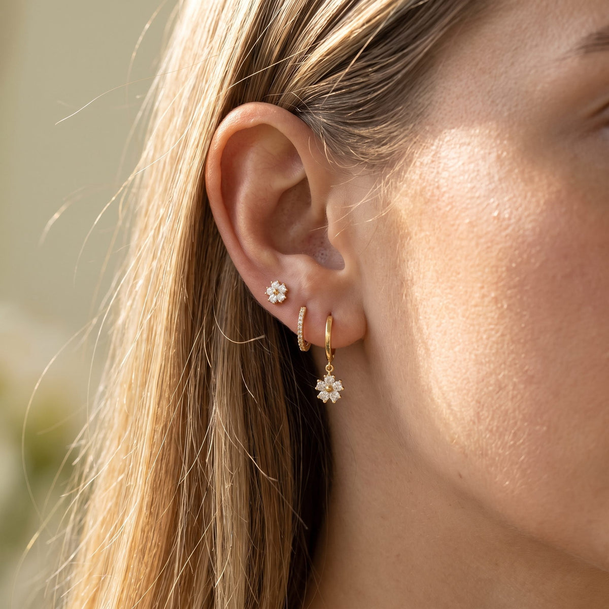 Close view of a woman wearing the Lilly Crystal Flower Earrings Set with gold flower charms on the lobe