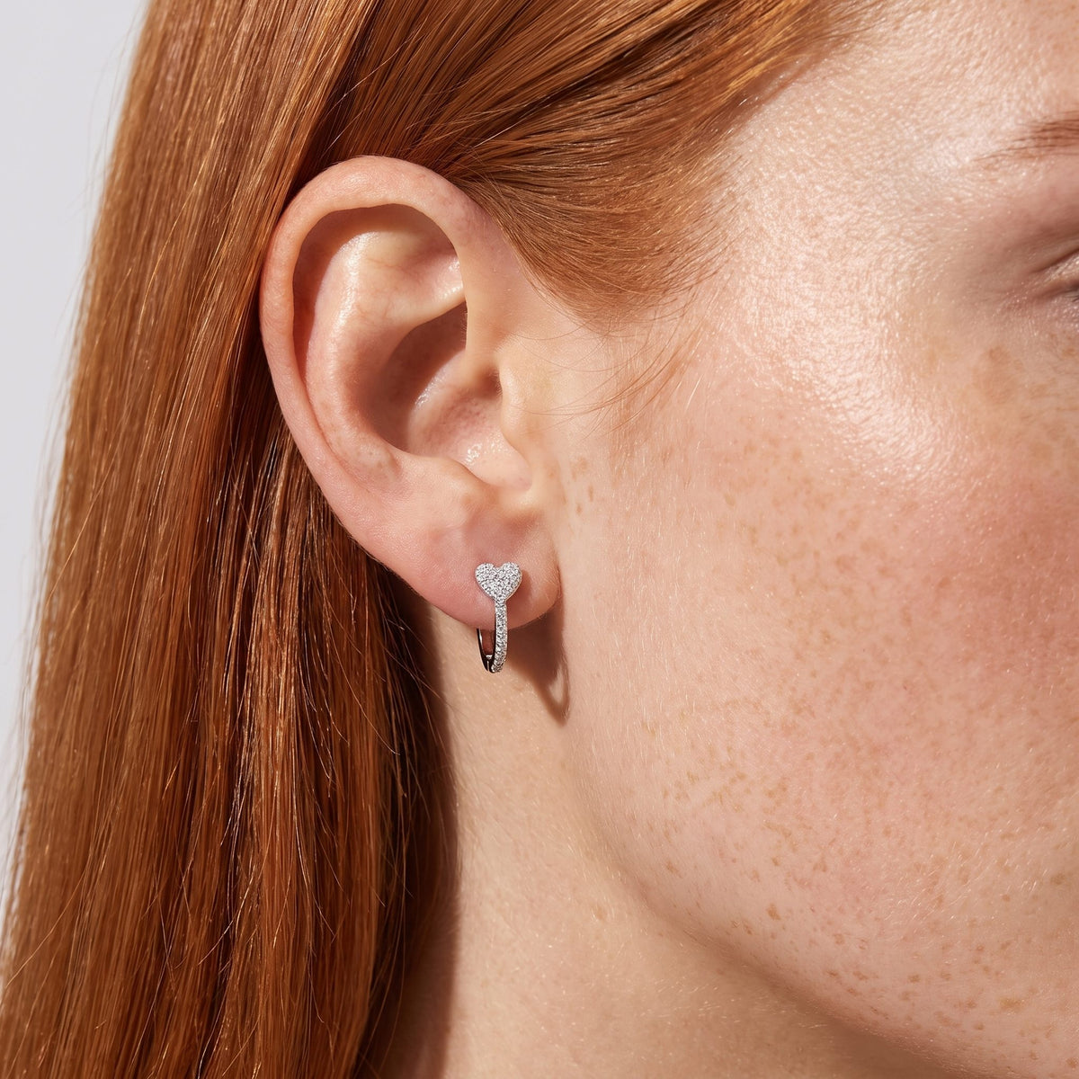 Woman wearing the Lilou Silver Heart Hoops featuring a crystal-paved heart sitting flat to the lobe