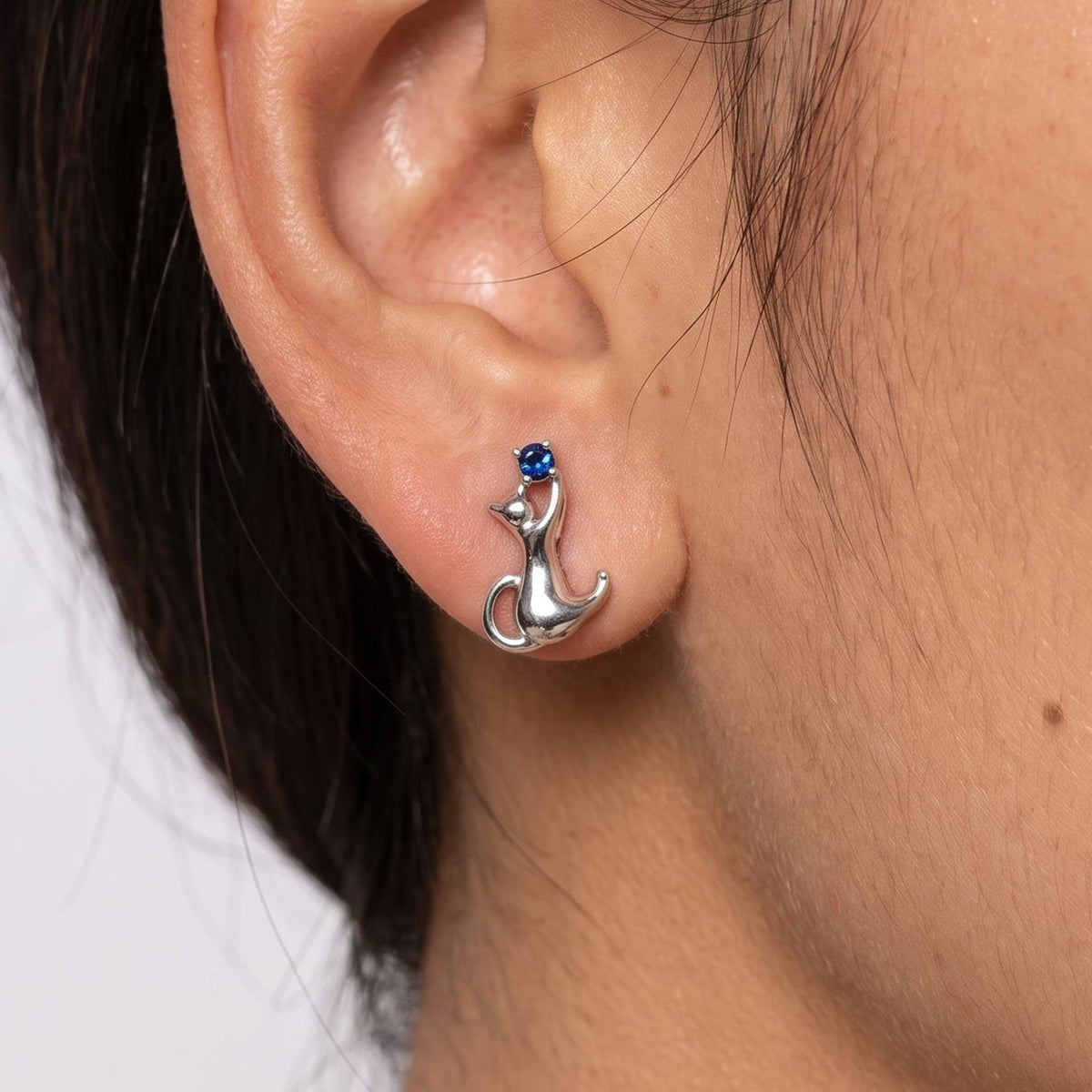 Woman wearing the Lilou Silver Kitten Earrings on her lobe, featuring a silver cat shape with a blue stone