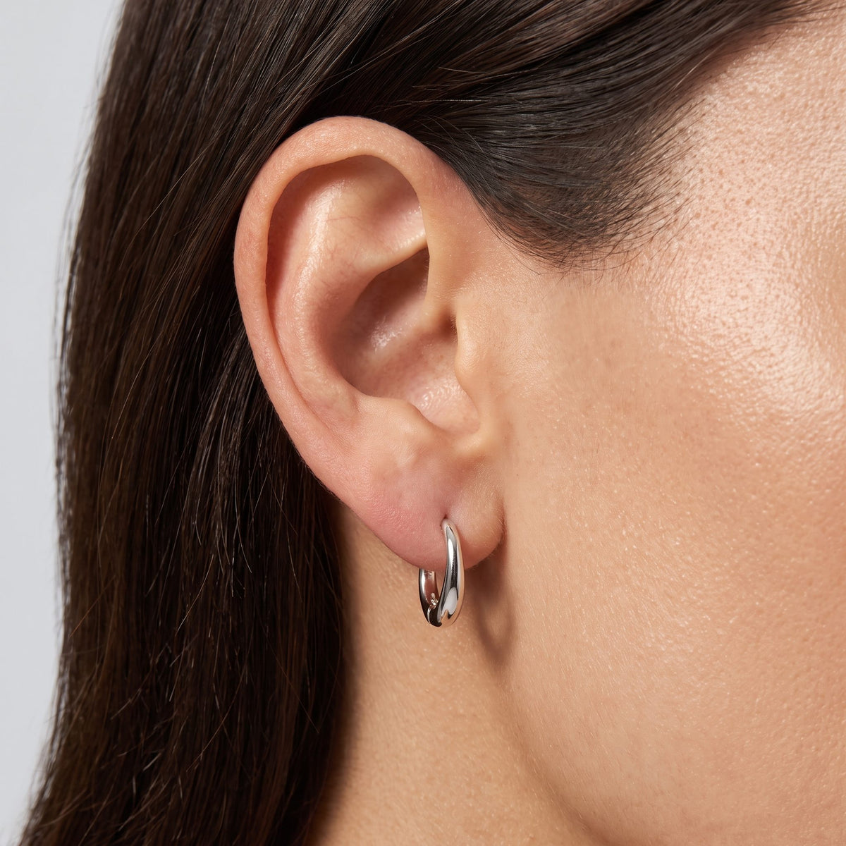 Woman wearing the Lilou Silver Wave Hoops through her lobe, showcasing their polished wavy shape