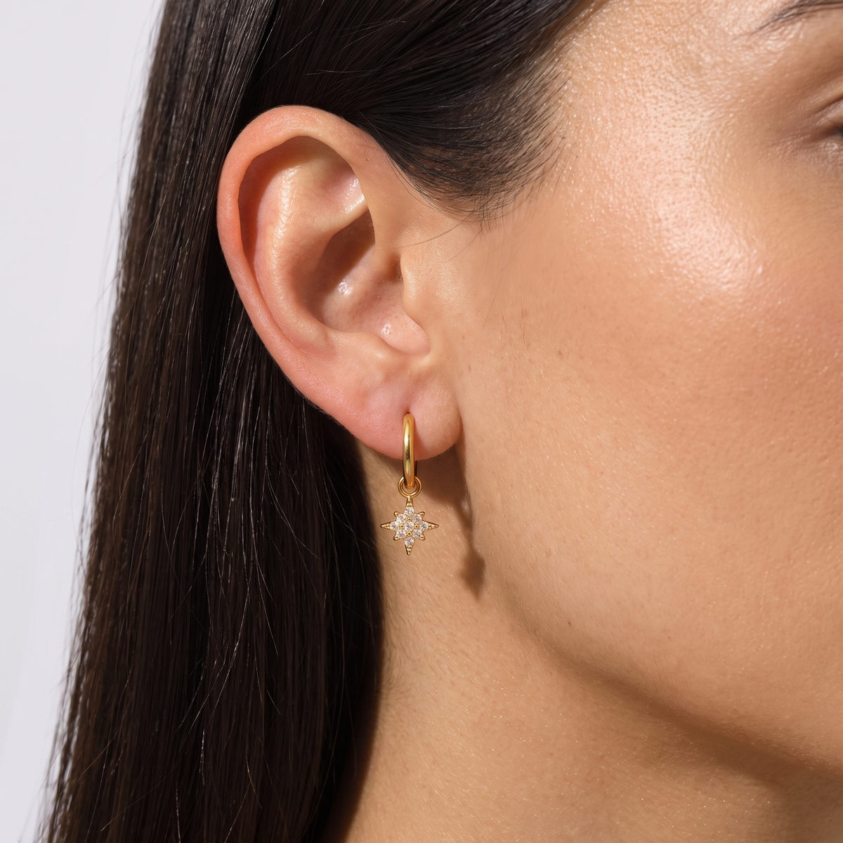 Close view of a woman wearing the Margaret Gold Earrings through the lobe, featuring a dangling starburst charm