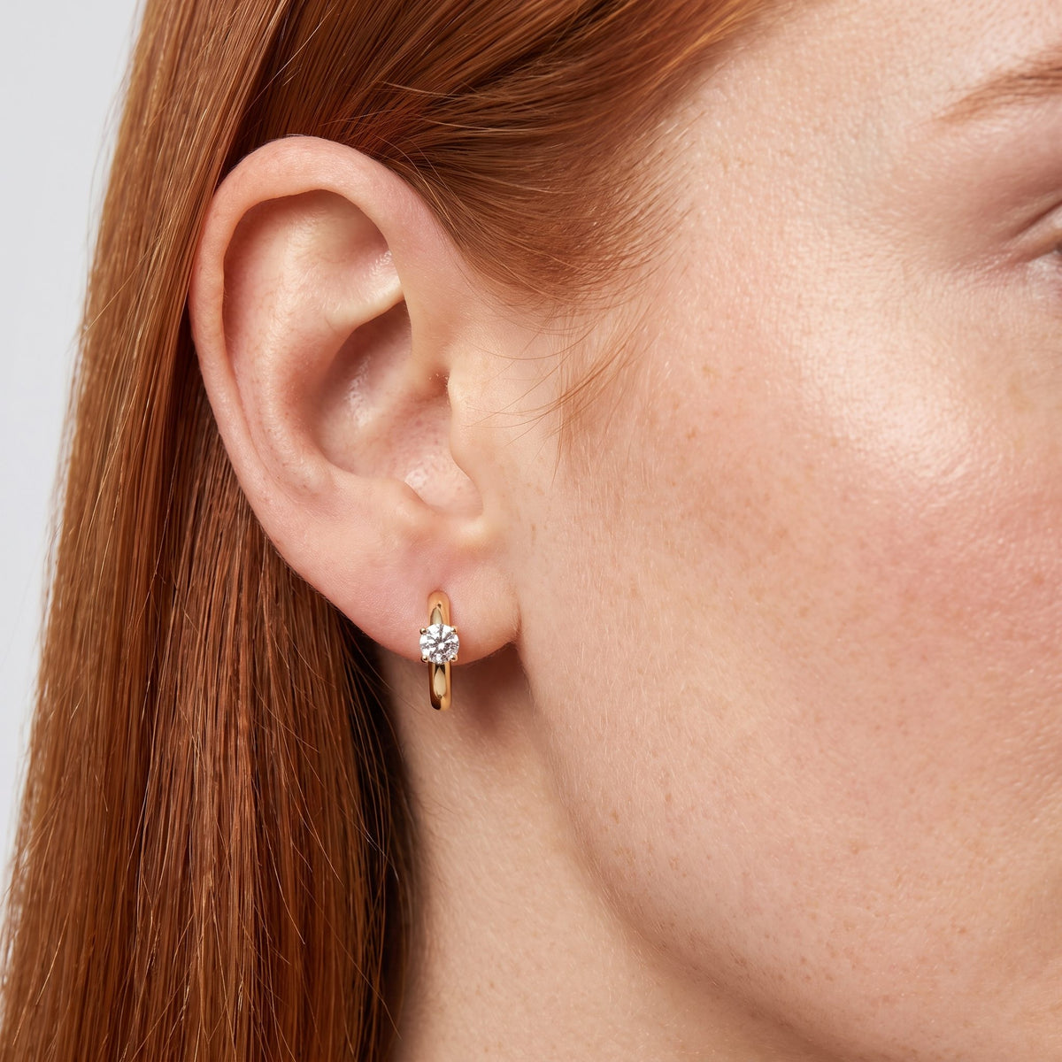 Woman wearing the Morgana Pixie Earrings through the lobe, featuring a gold-colored hoop with a single clear stone