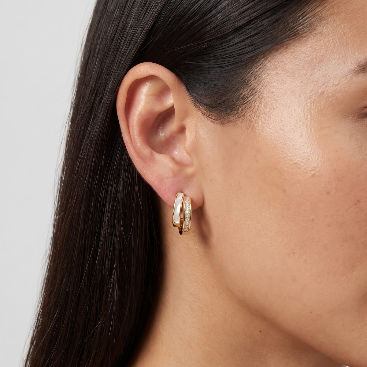 Woman wearing the Olivia Pearl & Crystal Earrings on her lobe, featuring a double gold hoop design
