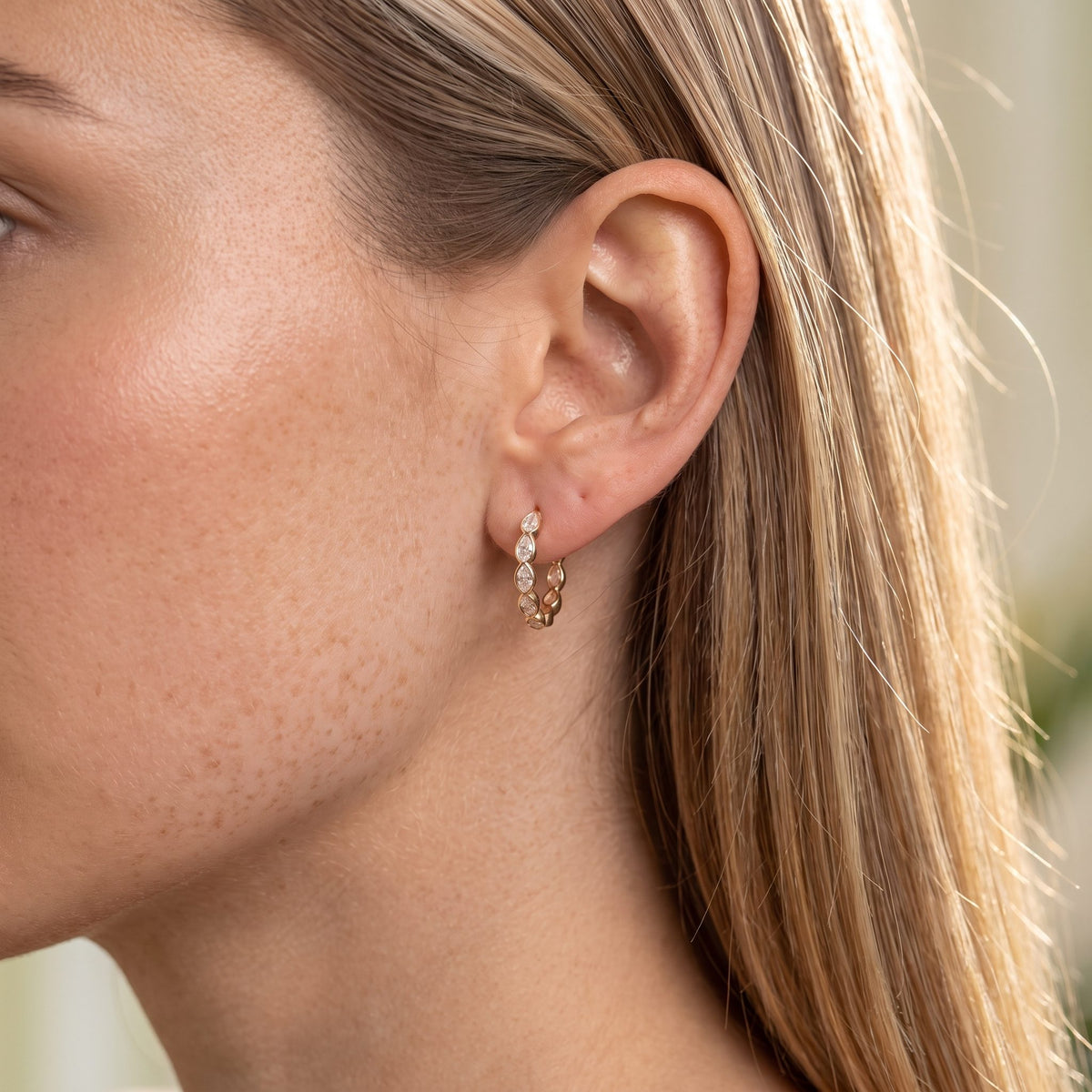 Woman wearing the Pear Bezel Hoops on the ear, with her straight blonde hair tucked back