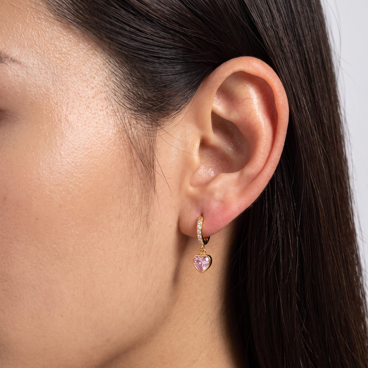 Woman wearing the Pink Heart Huggies on her ear, with her dark hair tucked behind it