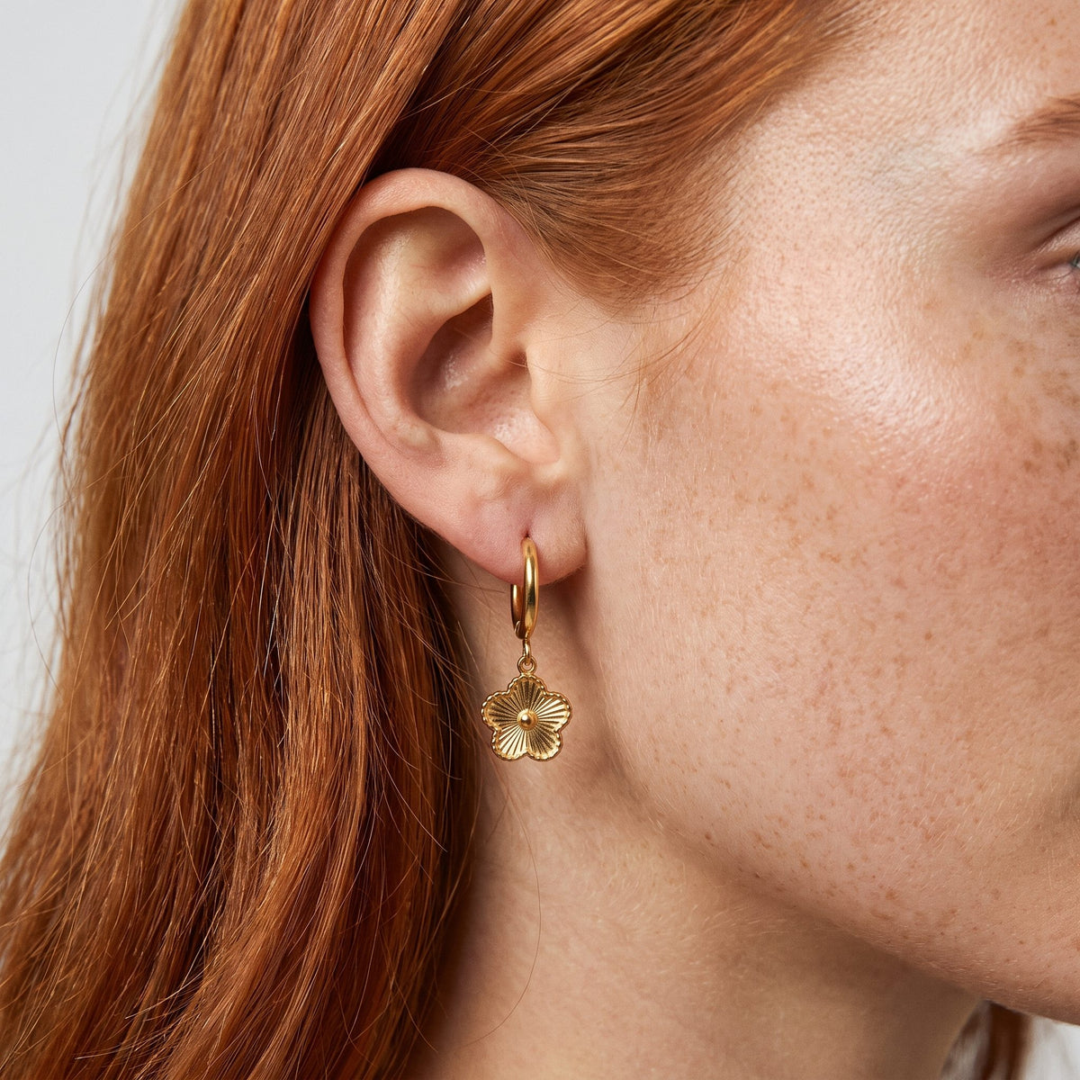 Woman wearing the Rowena Flower Hoop Earrings hanging below the lobe with a gold textured flower charm