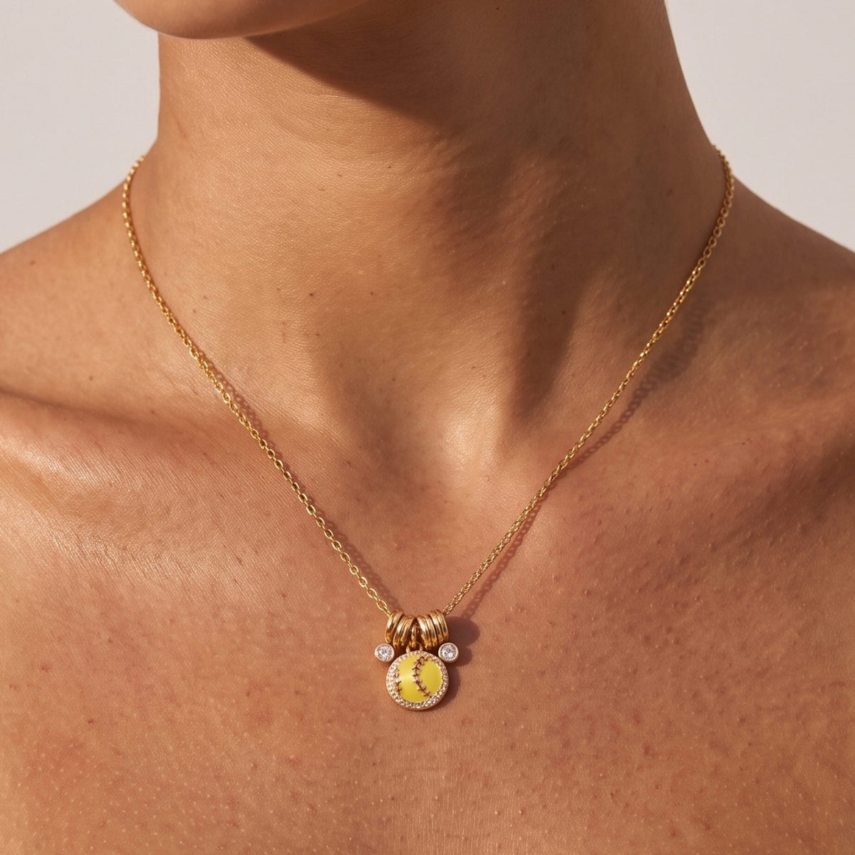 Close-up of the Softball Charm Necklace at the collarbone, featuring a yellow softball pendant set with small crystals