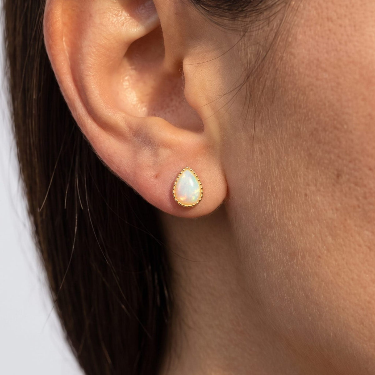 Woman wearing the Teadora Opal Teardrop Earrings on the lobe with a gold-colored frame