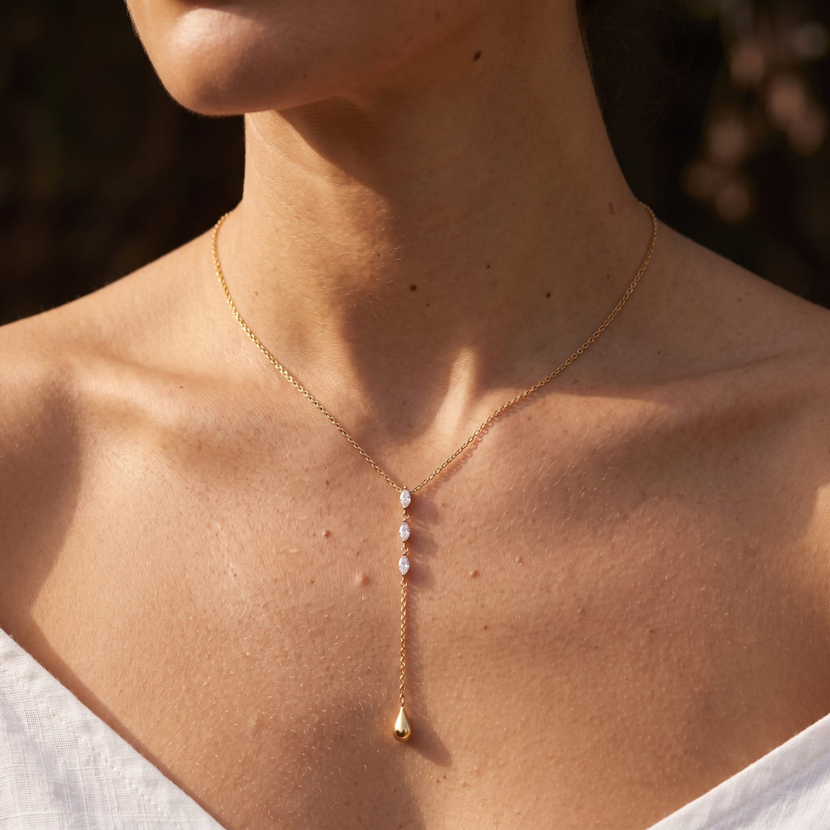 Woman wearing the Teardrop Lariat Necklace at the collarbone in warm sunlight