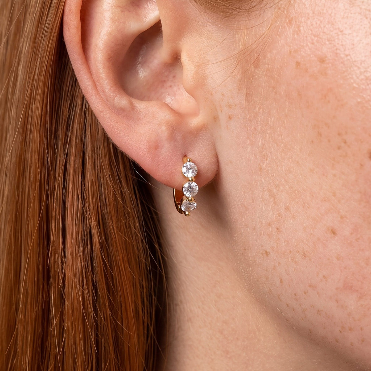 Close-up of the Three Stone Hoops on the ear, showing three clear crystals in a gold setting