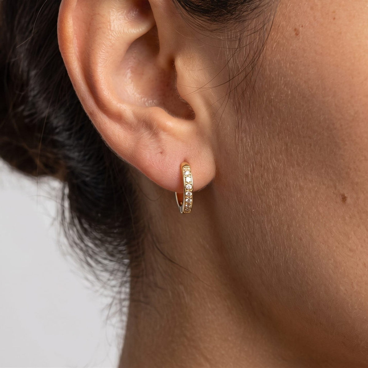 Woman wearing the Tina Hoop Earrings through the lobe, featuring a small gold-colored hoop with tiny crystals
