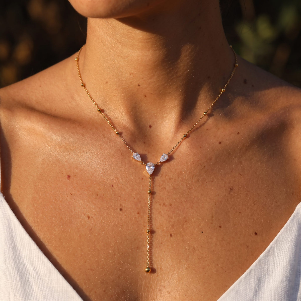 Woman wearing the Trefoil Lariat Necklace at the collarbone in warm sunlight