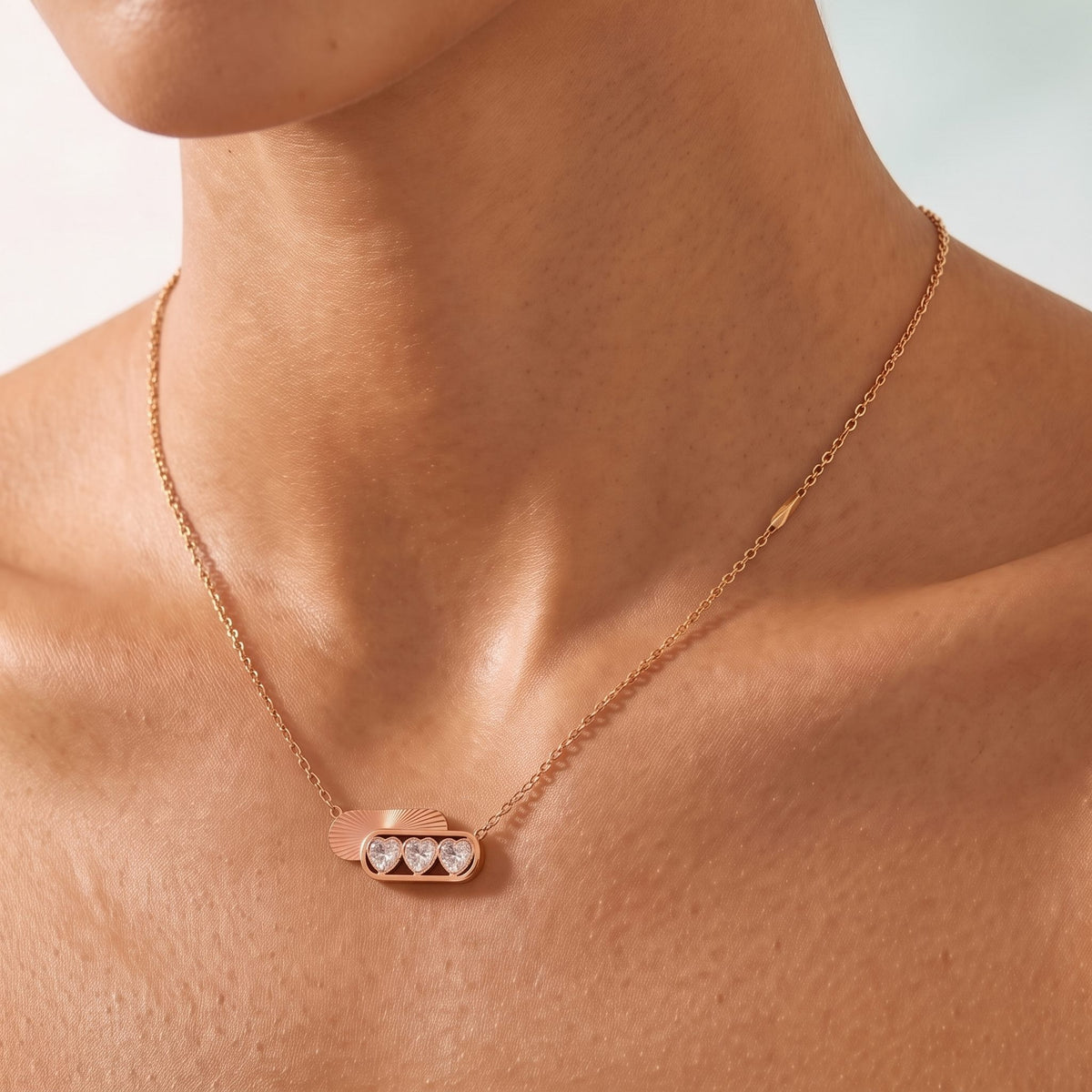 Close-up of the Triple Heart Necklace at the collarbone showing three sparkling heart crystals, in rose gold
