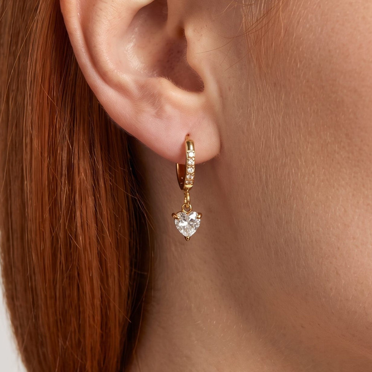 Woman wearing the Vittoria Crystal Heart Gold Earrings hanging below the lobe with a dangling heart crystal