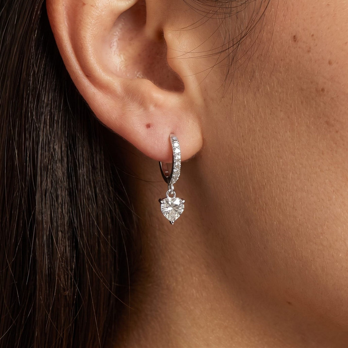 Woman wearing the Vittoria Crystal Heart Silver Earrings hanging below the lobe with a dangling heart-shaped crystal