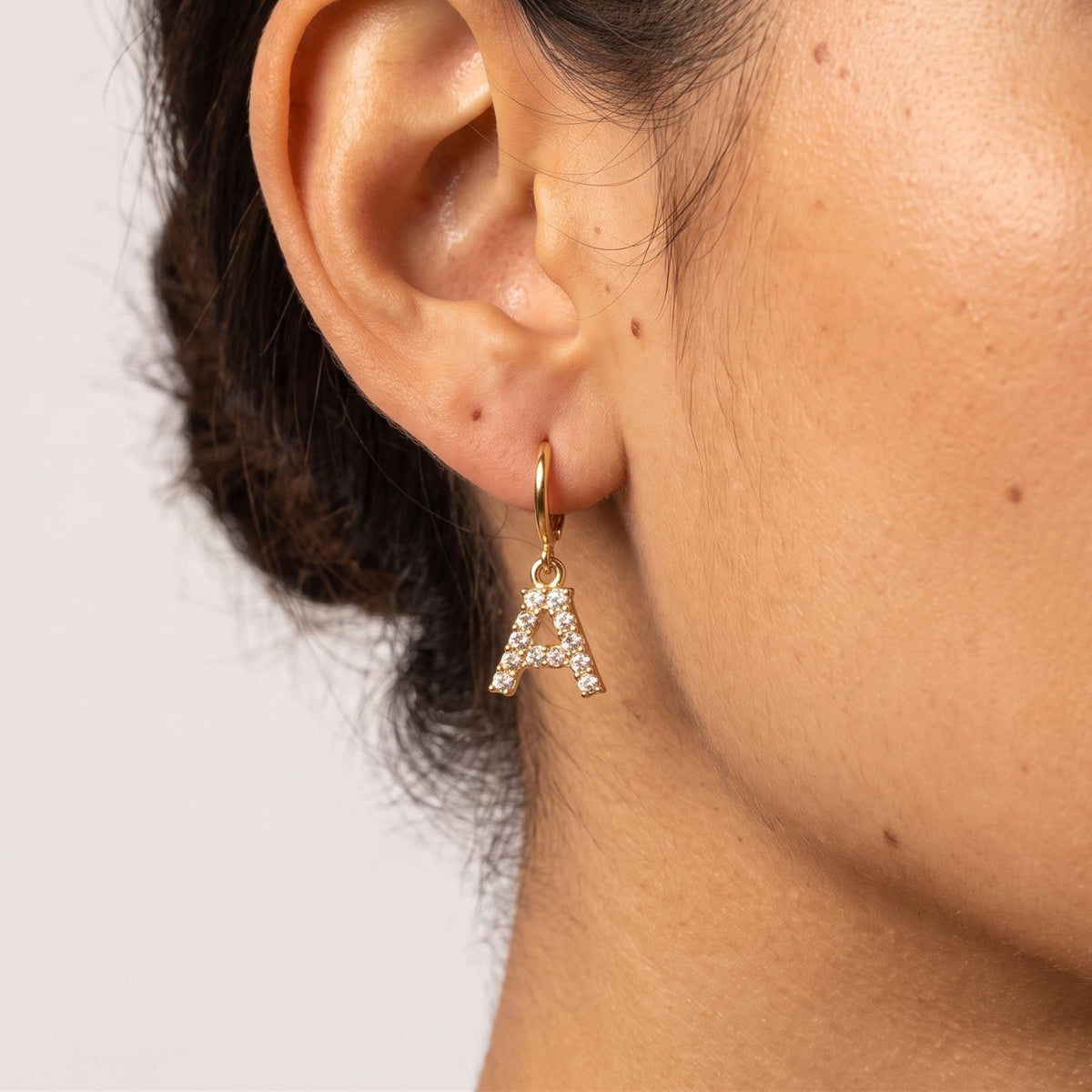 Woman wearing the Wilhemina Initial Letter Earrings featuring a crystal letter A charm hanging below the lobe