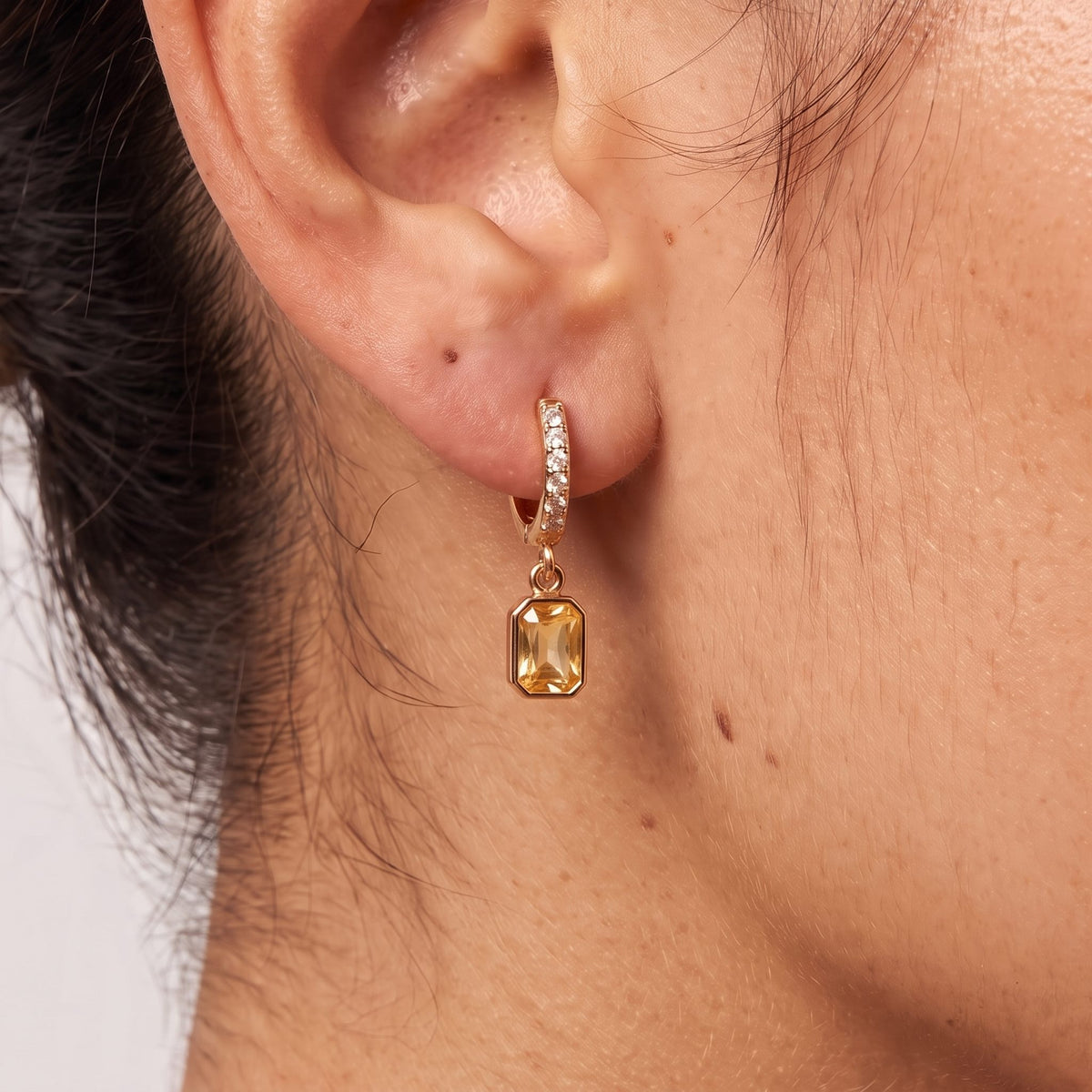 Close-up of the Yellow Octagon Huggies on the ear showing a yellow crystal charm, in rose gold